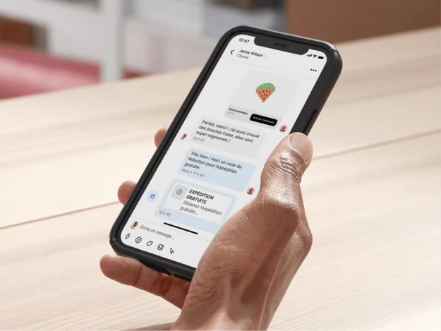 Une entrepreneuse est assise à son bureau et utilise Shopify Inbox sur son appareil mobile pour échanger avec un client. Elle partage un code de réduction dans le chat pour conclure la vente.
