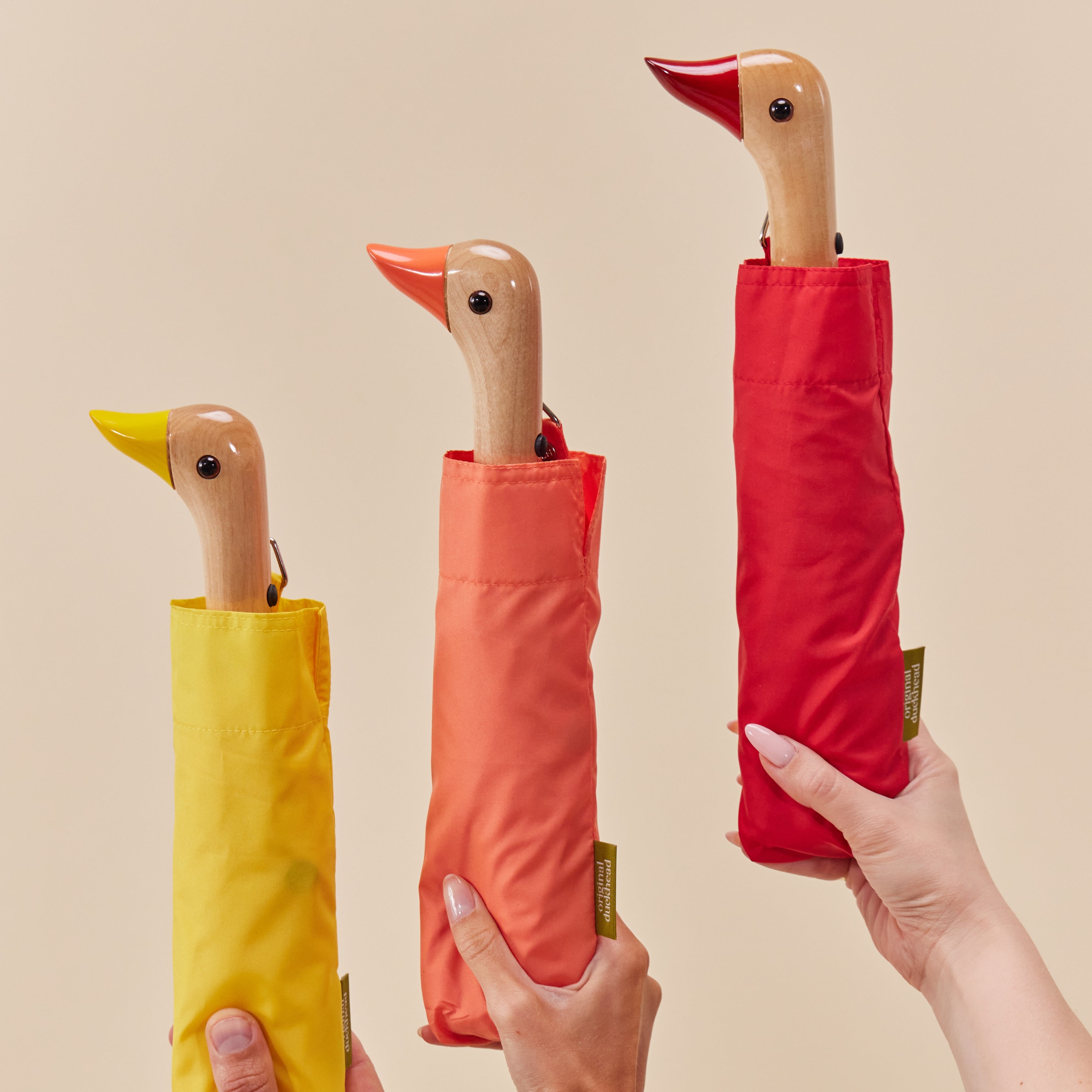 Original Duckhead umbrellas held by a model’s hand, pictured from left to right: Yellow, Peach, and Red.