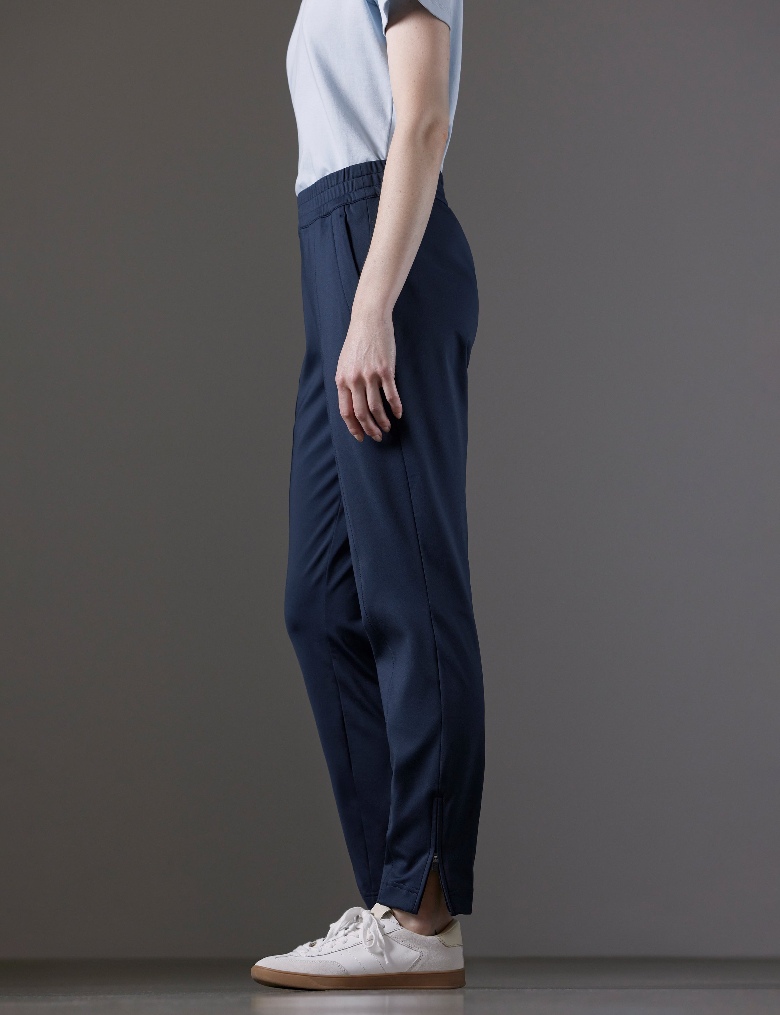 Side profile lower body view of woman wearing Eloise Travel Slim Pant in Total Eclipse dark blue from AETHER Apparel.