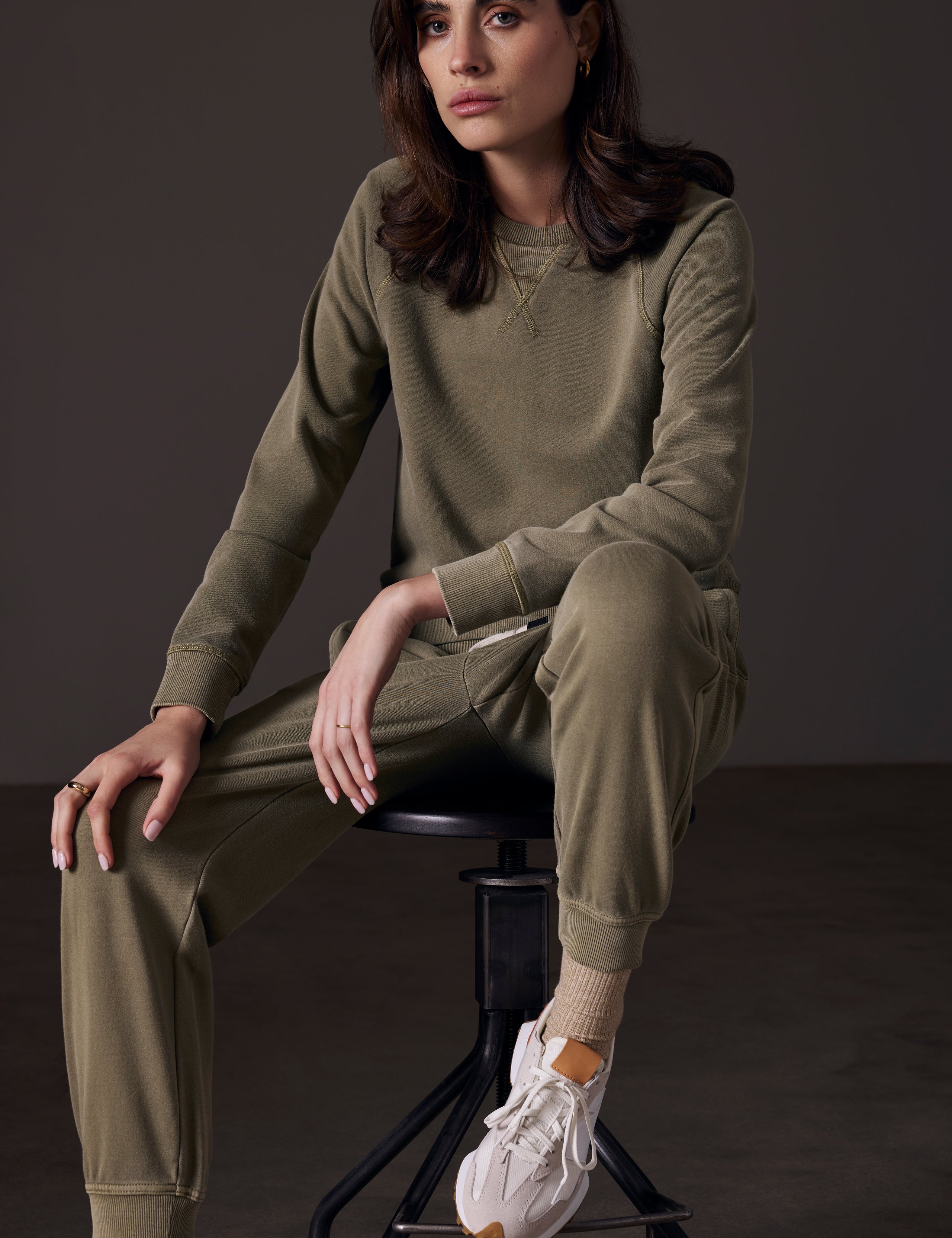 Front angled view of woman sitting on stool wearing Solstice Lightweight Jogger in Command Green from AETHER Apparel.