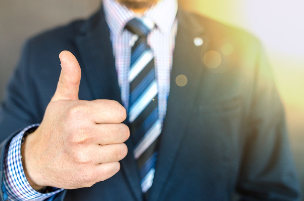 Torso of a man in a suit giving a thumbs up sign